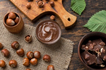 A bowl of hazelnut chocolate spread, surrounded by raw hazelnuts